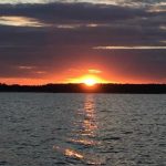 A serene sunset over a calm body of water, with vibrant orange and purple hues in the sky.